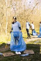 gemeenschap onderhoud vrijwilliger vermindert verspilling en reinigt omhoog Woud instelling, verzamelen vuilnis in blauw uitschot Tassen. jong kind helpt milieu behoud door weggooien van plastic afval. foto