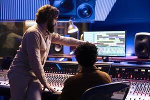 geschoold musicus werken met audio ingenieur naar Bewerk nieuw opgenomen sporen in controle kamer, drukken toetsen en faders Aan paneel bord bureau. team van artiest en producent creëren muziek- in studio. foto