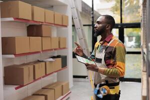 pakhuis werknemer gebruik makend van voorraad app Aan digitaal tablet voor goederen beheer. Afrikaanse Amerikaans magazijn manager vervelend beschermend industrieel algemeen analyseren online checklist foto