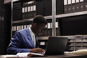 Afrikaanse Amerikaans zakenman analyseren administratief bestanden, lezing boekhouding verslag doen van in zakelijke bewaarplaats. boekhouder werken laat Bij nacht Bij bureaucratie Vermelding in opslagruimte kamer foto