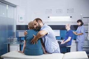 verpleegster in blauw scrubs behandelen oud vrouw met terug en wervelkolom pijn voor fysiek herstel. chiropractie dokter geven bijstand naar gepensioneerd geduldig met spinal koord letsel en orthopedische zorg. foto