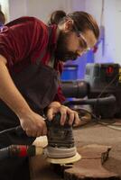 meubelmaker vervelend bescherming bril gebruik makend van hoek Slijper Aan hout naar glad oppervlakken door slijtage met schuurpapier. deskundige gebruik makend van orbital schuurmachine uitrusting voor meubilair in elkaar zetten baan in timmerwerk winkel foto