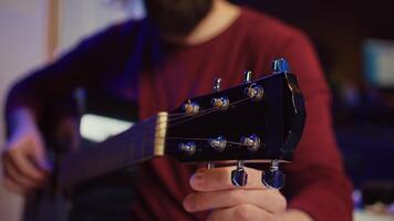 musical performer afstemmen zijn gitaar door draaien de knoppen, voorbereidingen treffen naar Speel akoestisch instrument in huis studio. artiest opname geluiden naar creëren nieuw spoor, gebruik makend van equalizer menging versnelling. camera b. foto