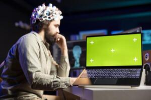 Mens met eeg koptelefoon Aan schrijven code naar overdracht geest in virtueel wereld, geïsoleerd scherm laptop Aan bureau transhumanistisch gebruik makend van neurowetenschappelijk tech en chroma sleutel notitieboekje naar krijgen superintelligentie foto