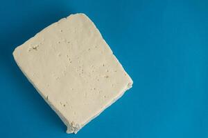 een blok van wit tofu zit tegen een helder blauw achtergrond, haar glad structuur en schoon randen creëren een gemakkelijk nog opvallend contrast. ideaal voor Gezondheid en plantaardig voedsel thema's. foto