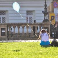 timisoara, Roemenië - juli 24, 2013 - een gelukkig mooi meisje Holding een wit ballon is zittend Aan de gras en ontspannende een zonnig dag in de stad foto