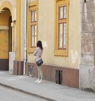 timisoara, Roemenië - april 13, 2014 - vrouw vervelend een zwart handtas is aan het wachten in de buurt een geel gebouw Aan de straat foto