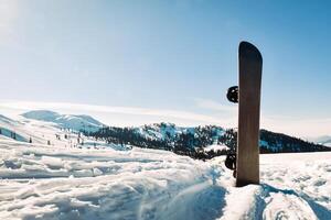 snowboard met zwart en wit stroken staand in sneeuw met winter bergen in achtergrond foto