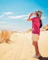 Kaukasisch vrouw dorstig drinken verkoudheid vers water in extreem warmte in heet wadi rum woestijn buitenshuis Aan wandelen spoor foto