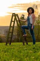een vrouw in tuinbroek met een ladder Aan een weide foto