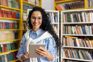 een vrolijk leerling gebruik makend van een digitaal tablet staat in een bibliotheek met een breed glimlach, omringd door schappen vol van boeken. foto