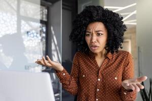 een Afrikaanse Amerikaans zakenvrouw verschijnt gefrustreerd terwijl pratend Aan een telefoongesprek. modern kantoor backdrop suggereert een professioneel instelling. foto