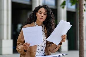 professioneel jong vrouw met gekruld haar- onderzoekt papieren gedurende een lunch breken door haar kantoor, belichamen bedrijf inzicht. foto