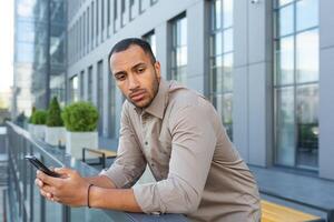 echt denken zakenman buiten kantoor gebouw nadenken beslissing, Afrikaanse Amerikaans arbeider verdrietig Holding telefoon in hand- foto