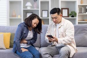 familie paar Mens en vrouw zittend Aan sofa Bij huis Aziatisch familie Mens proberen naar telefoontje dokter voor ziek vrouw. foto