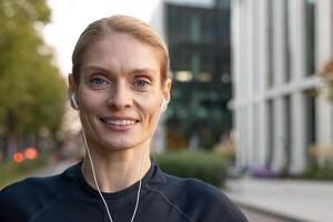 een glimlachen vrouw met oortelefoons in sportkleding is jogging door de stad Bij schemering, uitstralend Gezondheid en vitaliteit. foto