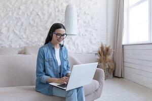 een jong vrouw leraar in een koptelefoon, Holding een laptop. werken, geeft les van huis online foto