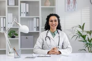 professioneel spaans vrouw dokter zittend Bij haar bureau met een stethoscoop, klaar naar begin een telefoontje in een kliniek kantoor instelling. foto