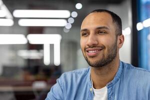 een professioneel spaans Mens met een vriendelijk houding gefotografeerd in een helder, hedendaags kantoor omgeving, overbrengen vertrouwen en positiviteit. foto