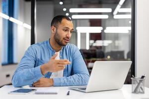 gefocust Indisch Mens in een blauw overhemd hebben een telefoontje in een goed verlicht modern kantoor, belichamen professionaliteit en inzet. foto