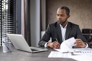 gefocust professioneel analyseren en werken Aan rapporten met laptop en kladblok in een modern kantoor instelling. foto