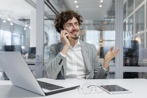 krullend haar jong professioneel Mens in een bedrijf instelling, actief verloofd in gesprek Aan een telefoon telefoongesprek. foto