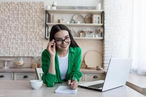 jong vrouw duurt aantekeningen in voorkant van laptop Bij huis. werken van huis. foto