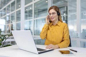 portret van een jong vrouw in een koptelefoon werken in een kantoor centrum online van een laptop. foto