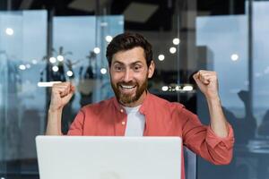 dichtbij omhoog van geslaagd zakenman, Mens vieren zege en geslaagd triomf, op zoek Bij laptop scherm lezing mooi zo nieuws en gelukkig Holding handen omhoog, winnaar gebaar foto