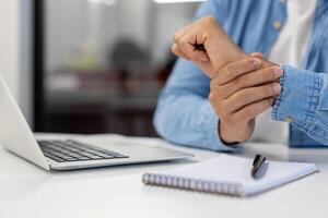 detailopname foto van spaans jong mannetje handen Holding polsen, gevoel erge, ernstige pijn terwijl zittend Bij werkplaats met laptop.