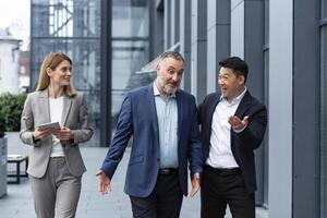 een verschillend team van het specialisten, senior en ervaren ingenieurs managers team leiders, een groep van drie arbeiders gelukkig wandelen buiten een kantoor gebouw, collega's in bedrijf pakken. foto