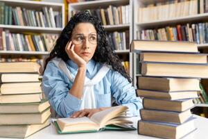 een attent en gefocust vrouw zit tussen een stapel van boeken in een bibliotheek, lezing en overweegt diep temidden van schappen gevulde met literatuur. foto