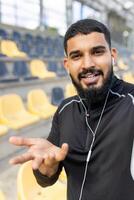 glimlachen Mens met oortelefoons bereiken uit Bij sport- stadion foto