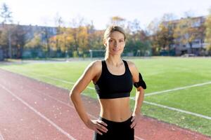 portret van volwassen volwassen vrouw atleet in stadion, vrouw atleet Holding handen Aan heupen glimlachen en op zoek Bij camera, jogging vrouw in trainingspak gedurende actief oefening en geschiktheid klas. foto