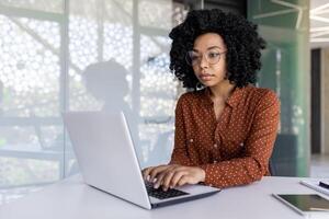 echt denken vrouw werken met laptop, typen Aan toetsenbord, denken geconcentreerd over oplossen stroom problemen, bedrijf vrouw geslaagd tevreden en zelfverzekerd Bij werkplaats binnen kantoor. foto