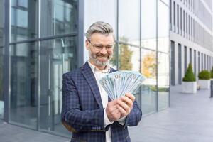ongelooflijk gelukkig zakenman houdt een stack van dollars in zijn handen, kan niet van mening zijn zijn geluk, glimlacht en looks Bij de geld. foto