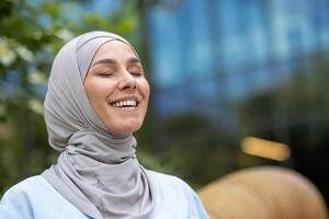 een beeld van een blij moslim vrouw vervelend een hijaab, lachend hartelijk buitenshuis met een wazig stad achtergrond. vangt een moment van oprecht geluk en vrijheid. foto
