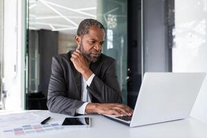 volwassen senior denken zakenman Bij werkplaats binnen kantoor, Afrikaanse Amerikaans grijs haren baas werken met laptop binnen kantoor. foto