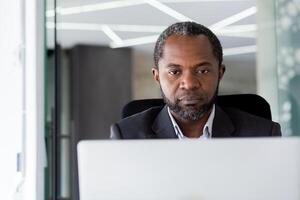 echt denken baas zakenman dichtbij omhoog, Afrikaanse Amerikaans Mens werken met laptop, Mens lezing van computer scherm concentreren en denken, Bij werkplaats binnen kantoor. foto
