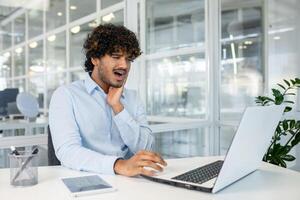 een Indisch professioneel ervaringen ongemak van een kiespijn terwijl werken Aan zijn laptop in een helder kantoor omgeving. de pijn verstoort zijn werk routine. foto