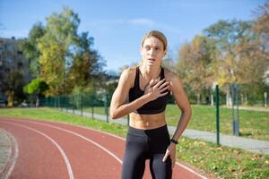 gefocust sportvrouw nemen een breken Aan rennen spoor, handen Aan knieën, gevoel uitputting na sprint. concept van bepaling en geschiktheid opleiding. foto