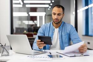 echt jong spaans mannetje accountant en accountant zittend in kantoor Bij bureau werken met documenten, rekeningen en rekenmachine. foto