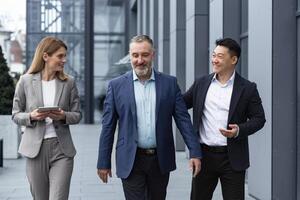 een verschillend team van het specialisten, senior en ervaren ingenieurs managers team leiders, een groep van drie arbeiders gelukkig wandelen buiten een kantoor gebouw, collega's in bedrijf pakken. foto