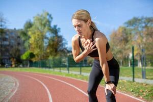 atletisch vrouw nemen een breken van een rennen Aan een zonnig dag, Holding haar knie en vangen haar adem Aan een spoor. foto
