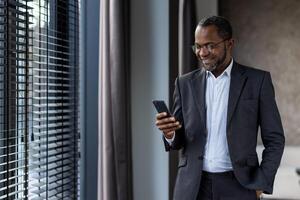 zelfverzekerd mannetje uitvoerend in een bedrijf pak verloofd met een mobiel telefoon, uitstralend geluk en professionaliteit. foto