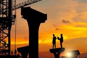 silhouet van ingenieur en arbeider team controle project Bij infrastructuur gebouw plaats, bouw plaats met wazig zonsondergang achtergrond foto