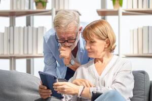 senior paar in leven kamer, vrouw en een Mens gebruik makend van tablet smartphone voor controle laatste nieuws, gelukkig familie concepten foto