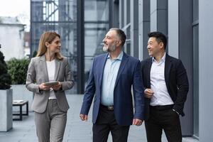 een verschillend team van het specialisten, senior en ervaren ingenieurs managers team leiders, een groep van drie arbeiders gelukkig wandelen buiten een kantoor gebouw, collega's in bedrijf pakken. foto