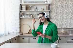 mooi jong vrouw in bril en groen overhemd ontspannende Bij huis in keuken, luisteren muziek- foto