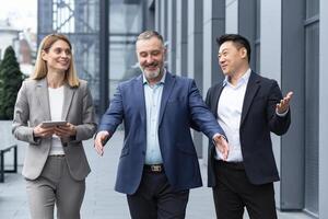 een verschillend team van het specialisten, senior en ervaren ingenieurs managers team leiders, een groep van drie arbeiders gelukkig wandelen buiten een kantoor gebouw, collega's in bedrijf pakken. foto